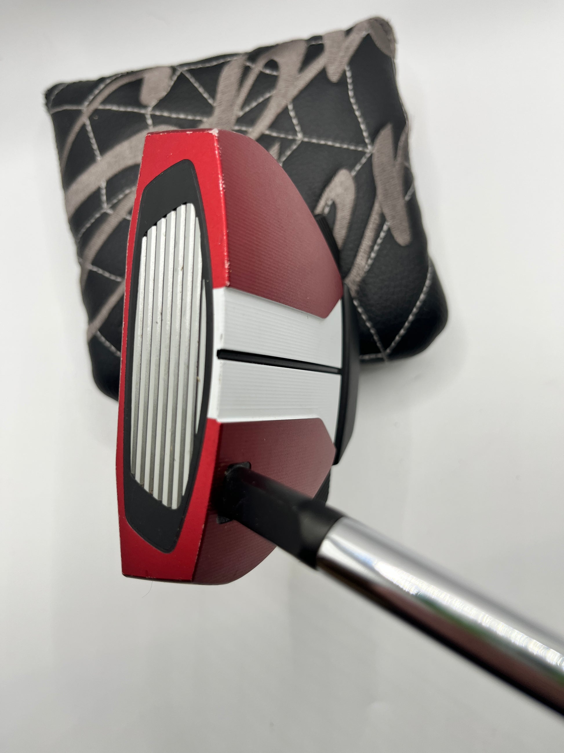 Golf putter with red and silver head and black and gray club head cover on a white background