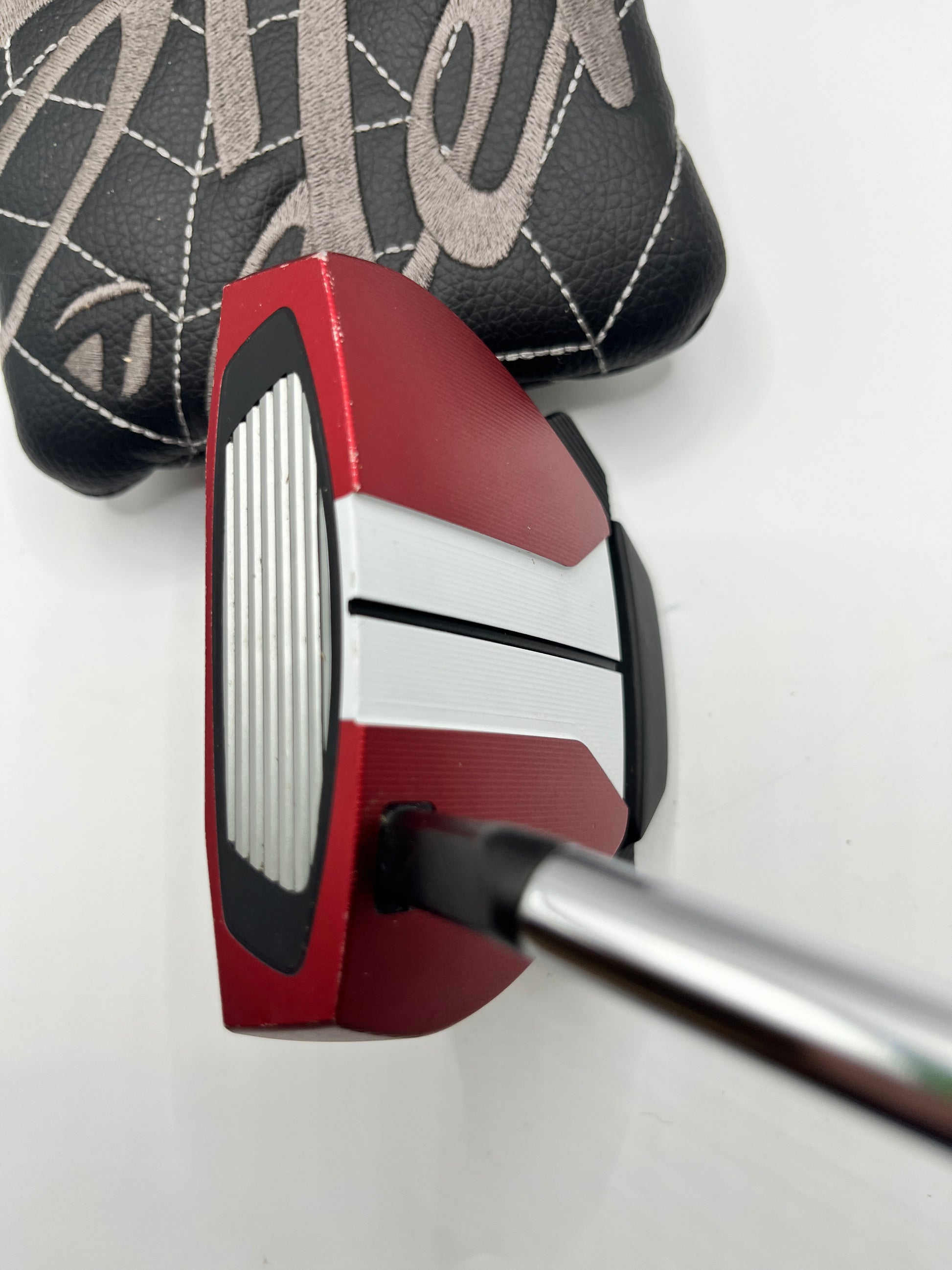 Red and white golf putter with black grip on a white background