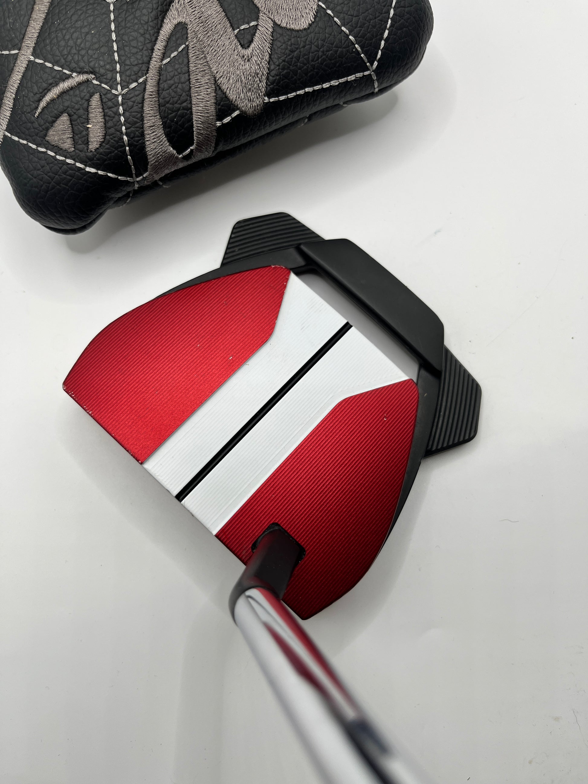 Golf putter with red and black head cover on a white background